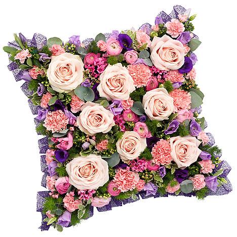 An image of the Pink and Mauve Cushion flower arrangement, featuring an array of pastel pink roses, chrysanthemums, and carnations, arranged in a cushion shape and adorned with a prominent purple ribbon, creating a lively and charming tribute